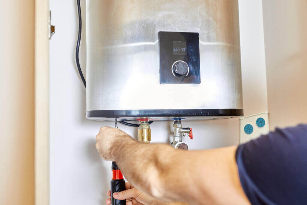 A man is fixing an electric water heater by tightening the pipe nut.
